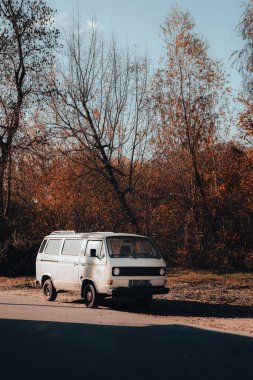 Sonbahar ağaçlarının altında park edilmiş klasik beyaz minibüs sonbaharda nostaljik ve yolculuğa hazır bir anı yakalıyor..