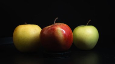 Koyu bir zıtlık ve tazeliği vurgulayan üç farklı renkte elma..
