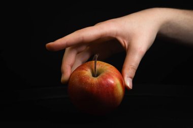 Kırmızı bir elmayı nazikçe siyah bir arkaplana doğru tutan bir el, basitlik ve zarafet hissi yaratır..