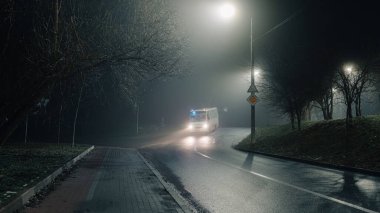 Islak asfalt ile sessiz gece yol sahnesi yoğun bir sis altında sokak lambaları yansıtan, kentsel ya da siyah-esinlenilmiş görseller için mükemmel.
