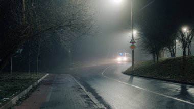 Islak asfalt ile sessiz gece yol sahnesi yoğun bir sis altında sokak lambaları yansıtan, kentsel ya da siyah-esinlenilmiş görseller için mükemmel.