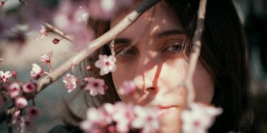 Kiraz çiçekleriyle çerçevelenmiş bir kadının yumuşak doğal portresi. Hassas ışıklandırma ve sığ alan derinliği ruhani bir bahar havası yaratır..