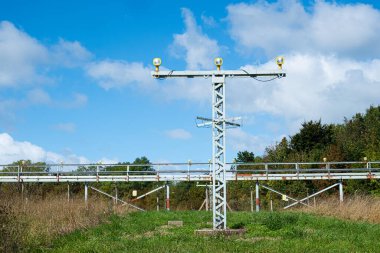 Pistin sonundaki yeşil bir alanda havaalanı yaklaşım ışıkları. Arka planda bir kirişe yerleştirilmiş bir sıra ışık ve ön tarafta mavi bulutlu bir gökyüzüne karşı alçak açıyla çekilen daha uzun bir metal kule var.
