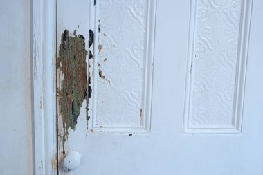 Büyük bir köpeğin sebep olduğu eski bir iç kapıda hasar var. Boya ve ahşap üzerinde çizikler var. Eski boyaların bir çok katmanı görünüyor..