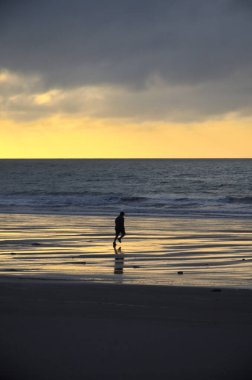 Sabah gün batımında kumsalda siyah elbiseli bir adam.