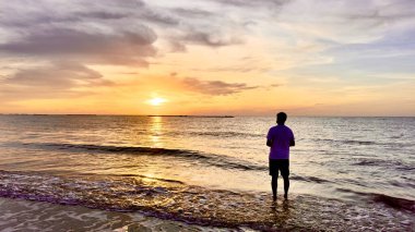 Genç bir adam sahilde durup güneşin batışını seyrediyor. Etrafı, o anın güzelliğini ve yalnızlığını yansıtan melankolik bir atmosferle çevrili..