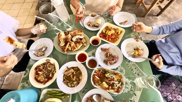 Bir anne ve iki oğuldan oluşan bir aile, lezzetli geleneksel Isaan yemeklerini yemek için bir araya geldi. İçinde domuz ızgarası, kızarmış tavuk ve diğer yerel yemekler vardı. Birlikte sıcak bir atmosfer yaratıyor ve kültürel kutlama yapıyorlardı.