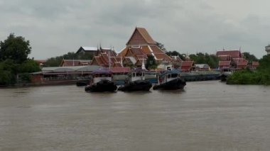 Üç römorkör nehir boyunca büyük bir kargo gemisini çekmek için birlikte çalışıyor. Arka planda endüstriyel taşımacılık ve kültürel manzara karışımı nehir boyunca seyahat ve ticari fotoğrafçılık için ideal.