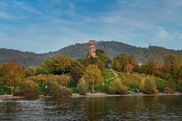 Sonbaharın son sıcak günleri. İnsanlar, Freiburgs Seepark 'ta sonbahar renkleriyle çevrili güneşli bir tepede sıcaklığın tadını çıkarıyorlar..