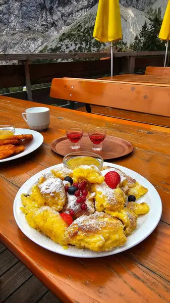 Kaiserschmarrn. Elma soslu, çilekli, üzümlü ve yaban mersinli Alman tatlısı. Pudra şekerli olsun. Bavyera Alplerinde bir restoran..