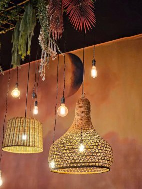 Lambalar ve dantel kolye avizelerden oluşan aydınlatma paneli, arka plandaki turuncu / kırmızı tonlar nedeniyle sıcak bir ortam tanımlıyor