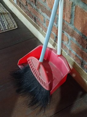 Kırmızı bir faraş ve süpürge kırsal bir tuğla duvara yaslanmış, rahat ve pratik bir temizlik düzeneği yaratıyor. Oda servisi ve temizlik için mükemmel..