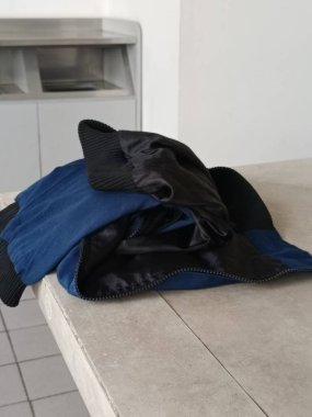 Günlük mavi ve siyah bir ceket gri bir masanın üzerinde, basitliği ve günlük modayı yansıtıyor. Günlük tarz, moda ve çamaşır konuları için ideal.