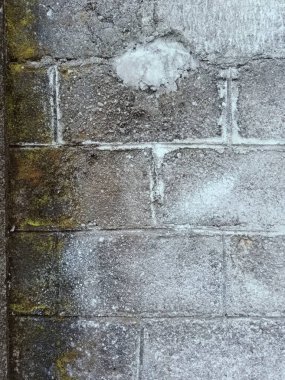 Birkaç renk lekesi olan gri ve beyaz bir duvar. Duvar betondan yapılmış ve pürüzlü bir dokusu var.