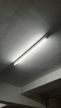 Basit bir floresan ışığı, minimalist endüstriyel alanda aydınlatma sağlar. Görüntü, yumuşak ışıklandırma efektleriyle temiz ve modern bir tavan yakalıyor..