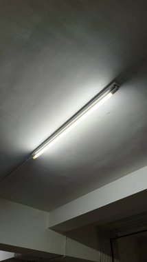 Basit bir floresan ışığı, minimalist endüstriyel alanda aydınlatma sağlar. Görüntü, yumuşak ışıklandırma efektleriyle temiz ve modern bir tavan yakalıyor..