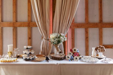 Çekici turtalar, kapkekler, çiçek aranjmanları ve ev içi dekoratif unsurların misafirler için hazır olduğu bir tatlı masası..