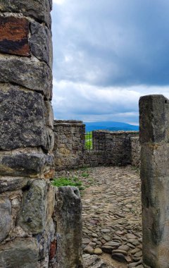 Uzaktaki tepelere bakan antik bir taş kalıntısının fotoğrafı. Kaba taşlardan yapılmış devasa duvarlar mahremiyet ve terk edilme hissi yaratıyor..