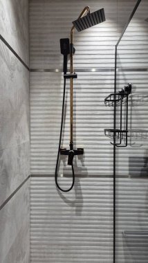 Dikey duvarların arkasında zarif bir duş odası görülebilir ve düzgün raflarla tamamlanır. Temiz çizgiler ve minimalist tasarım