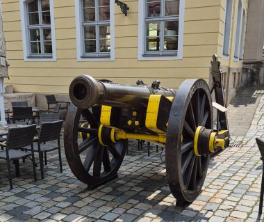 Tekerleklere monte edilmiş ve parlak renklerle boyanmış antik bir top var. Sokak kafeleriyle çevrili taştan bir üste yer almaktadır.