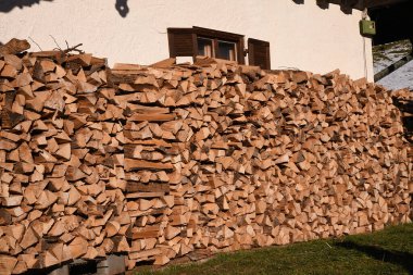 Bir evin duvarına istiflenmiş bir odun yığını. Arka planda kapalı panjurlu bir pencere görebilirsiniz.