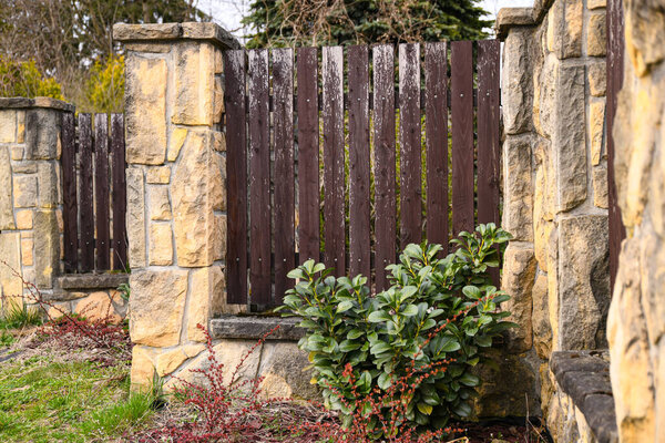 Close-up of a fragment of a stone fence with wooden sections. The fence consists of massive pillars lined with uneven light stone and brown wooden sections
