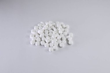 Görüntü, beyaz yuvarlak tabletlerden oluşan küçük bir yığını gösteriyor. Tek bir ışık arka planına rastgele dağılmış.