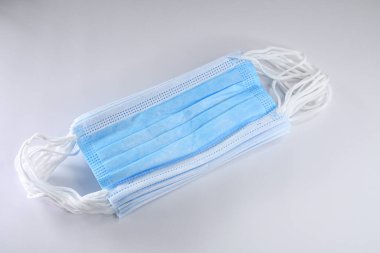 Fotoğrafta düz bir arkaplanda duran yeni, kullanılmamış mavi tıbbi maske yığını görülüyor..