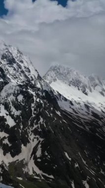 Önünde kıvrılan kış tepeleri olan karlı dağ zirveleri.