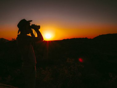 Safari günbatımında dürbün kullanan bir erkek silueti altın ufkun huzur dolu güzelliğini ve huzur dolu vahşiliğini ön plana çıkarır.
