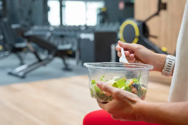 Spor salonunda bir kadın spor yaparken sağlıklı bir salata yiyor..