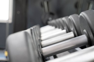 Arka planda bulanık bir spor salonu ortamında siyah ve gümüş renkli halterlerin yakın çekim görüntüsü.