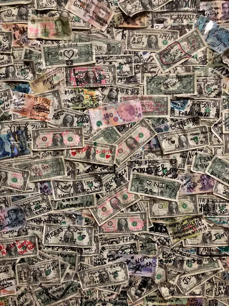 Tamamen Amerikan dolarları ile kaplı eşsiz bir duvar üzerinde çeşitli el yazısıyla yazılmış graffiti ve renkli detaylar var.