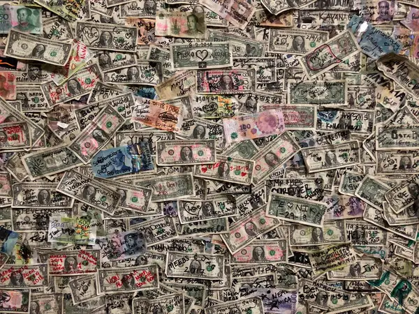 Tamamen Amerikan dolarları ile kaplı eşsiz bir duvar üzerinde çeşitli el yazısıyla yazılmış graffiti ve renkli detaylar var.
