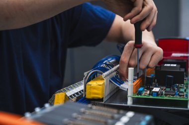 Endüstriyel elektrik kontrol paneli üzerinde çalışan teknisyenlerin yakın çekimi. Görüntü, mühendislik, elektrik, bakım ve otomasyon gibi kavramları temsil eden kablolar ve elektronik bileşenlerle yapılan elle yapılan hassas çalışmaları gösteriyor..