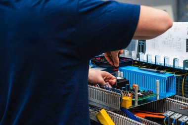 Endüstriyel elektrik kontrol paneli üzerinde çalışan teknisyenlerin yakın çekimi. Görüntü, mühendislik, elektrik, bakım ve otomasyon gibi kavramları temsil eden kablolar ve elektronik bileşenlerle yapılan elle yapılan hassas çalışmaları gösteriyor..