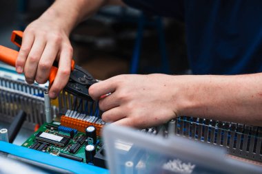 Endüstriyel elektrik kontrol paneli üzerinde çalışan teknisyenlerin yakın çekimi. Görüntü, mühendislik, elektrik, bakım ve otomasyon gibi kavramları temsil eden kablolar ve elektronik bileşenlerle yapılan elle yapılan hassas çalışmaları gösteriyor..