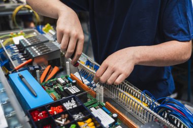 Endüstriyel elektrik kontrol paneli üzerinde çalışan teknisyenlerin yakın çekimi. Görüntü, mühendislik, elektrik, bakım ve otomasyon gibi kavramları temsil eden kablolar ve elektronik bileşenlerle yapılan elle yapılan hassas çalışmaları gösteriyor..