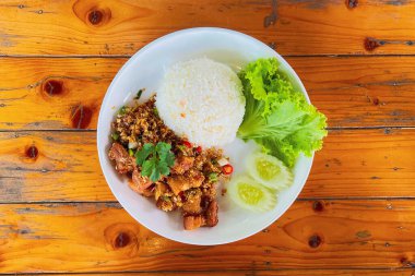 Tahta bir masada beyaz bir tabakta sarımsaklı pirinçli kızarmış domuz eti.