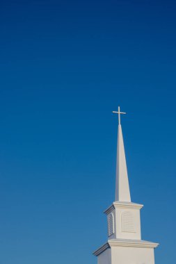 Tepesinde haç olan beyaz bir kilise kulesi canlı, bulutsuz mavi gökyüzüne karşı dimdik ayakta duruyor. İnancı ve huzuru simgeliyor..