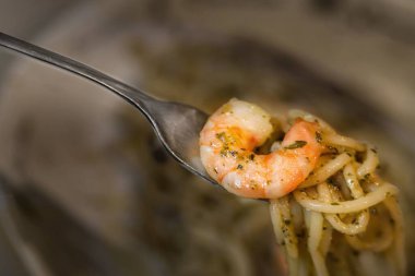 Bir çatal bir parça karides tutuyor. Karides bir tabak makarnanın üstünde.