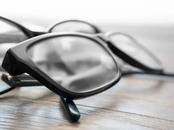 Kırsal bir ahşap yüzeyde iki çift siyah gözlük var. Şeffaf lensler yumuşak ışığı yansıtıyor, zarif bir atmosfer yaratıyor ve tasarımı üzerinde odaklanmalarını sağlıyor..