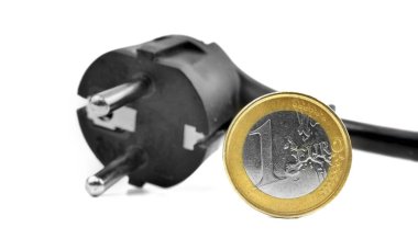 Siyah bir elektrik prizinin yanına yerleştirilen bir avroluk bozuk para, günlük yaşamda para ve enerji harcamaları arasındaki ilişkiyi vurguluyor. Görüntü maddi durumları gösteriyor..