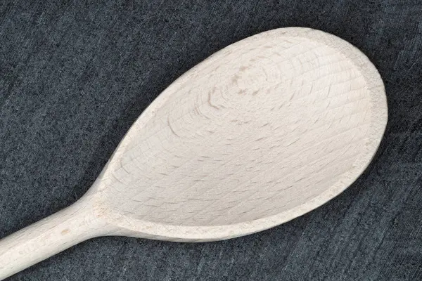 Çok güzel işlenmiş bir ahşap kaşık, pürüzsüz dokusu ve ince detaylarıyla karanlık bir taş yüzeyde duruyor. Doğal ahşap tanecikleri çekiciliğine ve benzersizliğine katkı sağlar..