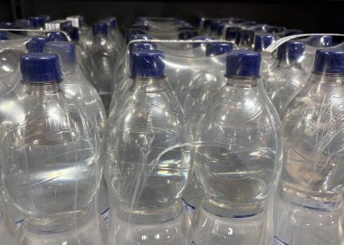 Bir perakende mağazasında saf plastik ambalajlar halinde dizilmiş sıra sıra şişe su. Temiz şişeler ışığı yansıtıyor, tazeliklerini ve satın alınmaya hazır olduklarını vurguluyor..