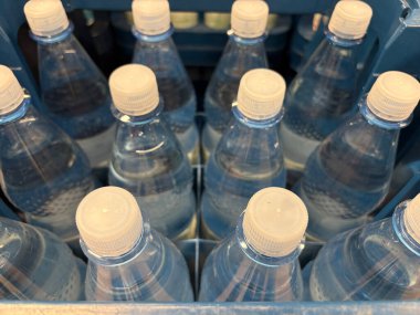 Mavi plastik bir sandığın içinde etiketleri ve kapakları sergilenen birden fazla temiz su şişesi var. Bu ayar bir pazar veya etkinlik için hazırlanmayı önerir.