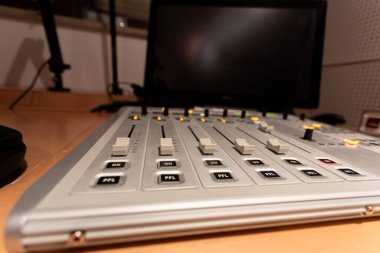 Stüdyo ortamında bir ses karıştırma konsolunun detaylı görüntüsü. Çeşitli sürgüler ve düğmeler çalışma alanını aydınlatır. Monitörler geceleri loş bir odada bilgileri görüntüler.