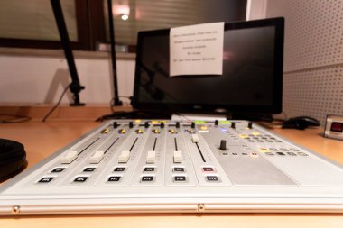 Bir yayın stüdyosunun kontrol odasında, ekipmanlarla çevrili bir ses karıştırma konsolu yanıyor. Çalışma alanı canlı yayın faaliyetleri için düzenlendi ve hazır..