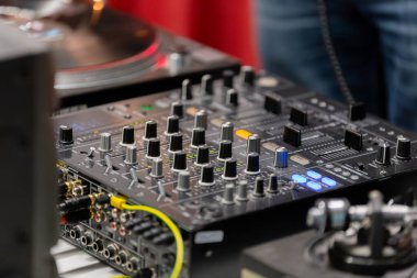 Ses ekipmanları aktif olarak bir etkinlikte DJ 'in müziği karıştırması gibi kullanılır. Kontrol düğmeleri ve kanalları ses manipülasyonunun karmaşıklığını gösteriyor. Misafirler canlı atmosferin tadını çıkarıyorlar..