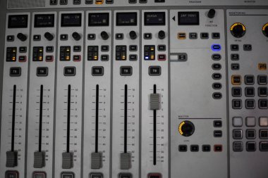 Loş bir mekanda canlı performans sırasında ses seviyelerini ayarlamak için kullanılan profesyonel bir ses karıştırma konsolunda birkaç fader ve düğme görülebilir.